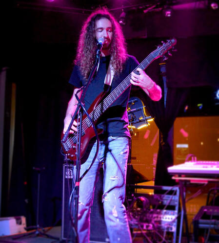 Man with long hair plays electric bass on a purple-lit stage