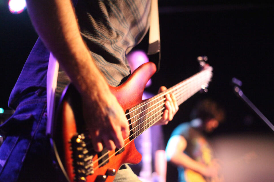 An electric bass is played on stage by a person whose body is mostly off screen